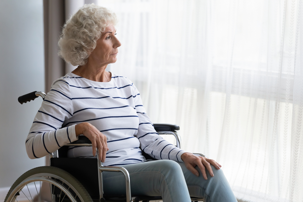 A thoughtful middle-aged old woman sitting in a wheelchair indoors.