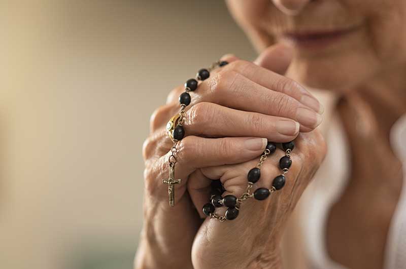 With a Christian necklace in her hands, an elderly woman says a prayer.