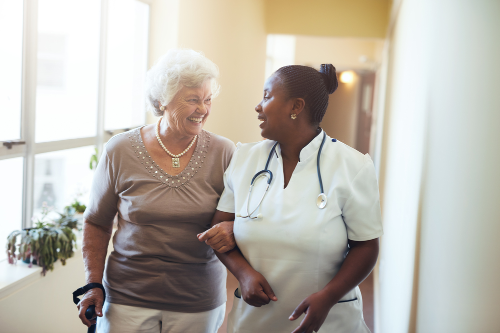 Senior woman walking in the nursing home supported by a nurse.